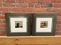 Front view of both framed paintings against brick background