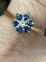 Close-up of ring worn on finger showing flower cluster design with central diamond and surrounding blue sapphires