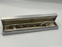 Full view of bracelet seated in its original rectangular silver-tone box lined with satin