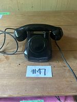 Front angled view of the black 1953 Monophone rotary telephone showing the handset and cord attached on wooden surface.