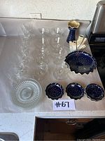 Overview of all glass and blue ceramic serving items on a white kitchen counter showing wine glasses, plates, bowls and vase.
