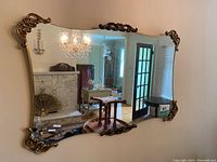 Large rectangular vintage mirror hung on a wall reflecting a living room with chandelier, marble fireplace, and wooden furniture.