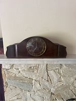 Front view of a wooden mantle clock showing the round glass-covered clock face with large gold Arabic numerals and hands.
