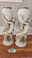 Front view of both matching classical style female figure plant stands with large urn planters, cream colored with gold trim and floral base.