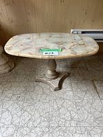 Front angled view of oval mosaic stone top coffee table against wooden panel wall, showing base and tabletop details