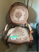 Front view of vintage needlepoint floral accent chair with carved wood frame and padded armrests showing upholstery and wood detailing.
