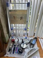 Photo of drying rack, clock, hangers, and assorted personal care items displayed on floor near window.