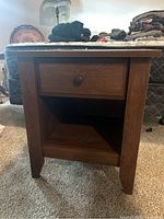 Front angle of a medium brown wooden nightstand showing single drawer with metal knob and open shelf below.