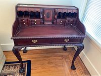 Full view of an antique wooden secretary desk showing wooden cubbies, drawers, and central cabinet with carved legs.
