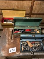 Image shows three metal tool boxes partly open, displaying the contents inside including various hand tools such as screwdrivers and wrenches.