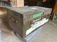 Side view of antique wooden and metal reinforced trunk with worn paint and a label showing Vancouver address.