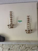 Pair of two matching wall sconces mounted on wall, each with three white taper candles and hanging crystal teardrops.