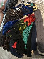 Photo showing a pile of women's dresses and shirts including dark brown velvet-like dress, blue crush velvet dress, black dress with floral and lace details, and grey dress.
