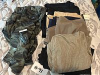 Multiple women's shirts, pants, and skirts bundled together on bed