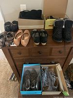 Full view of shoes on dresser including boots, flats, sneakers, some new in box.