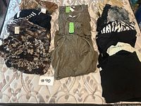 Lot overview photo showing all 13 women’s tops laid on mattress including various colors and patterns, with three identical green tops centered