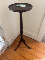 Front angle view of wood plant stand showing round top surface and turned column with tripod base.