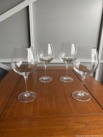 Front view of four clear wine glasses placed on a wooden table against a white background.