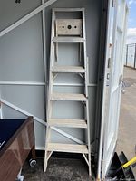 Front view of the aluminum step ladder leaning against a wall indoors, showing six steps and flat top platform.