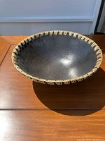 Top angled view showing black bowl with woven rim in natural beige color and shiny textured interior surface.
