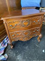 Front view of one of the hand-carved bedside tables showcasing detailed carving and metal drawer handles.