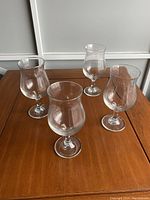 Four clear cocktail glasses displayed on a wooden surface showing their shape and design