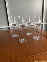 Four clear Lucaris crystal wine glasses with long stems and gently flared rims arranged on a wooden table, showcasing shape and clarity.