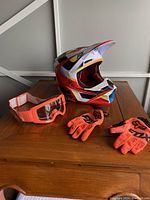 Side view of the Fox youth full-face motocross helmet, goggles, and gloves displayed on a wooden surface.