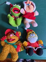 Four plush Happy Meal toys laid out including Kermit, Miss Piggy, Fozzie Bear, and Garfield Santa, showing front views and details.
