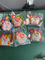 Six sealed TY Beanie Babies McDonald's Happy Meal toys in original packaging, laid out on a table. Each toy is a different character with distinct colors and the McDonald's Happy Meal logo on the packaging.