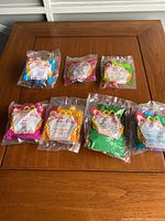 Wide view of 8 McDonald's Happy Meal toys from 1999 Doug Movie sealed in original colorful bags laid out on wooden table.