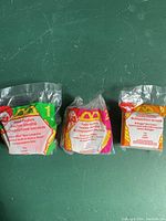 Three McDonald's Food Foolers Happy Meal toys still sealed in their original packaging, showing back of packages with McDonald's logo and multilingual descriptions.