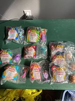 Full view of seven sealed McDonald's 1996 Hercules Happy Meal toys laid out on green surface. Shows packaging and character inserts clearly.