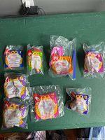 Seven unopened McDonald's Happy Meal toys from 1996 laid out in their original plastic packaging on a green surface.