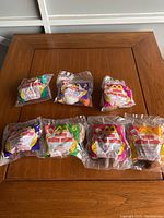 Photo of all eight McDonald's Lion King 2 Happy Meal toys in original sealed packaging, laid out on wooden table.