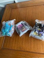 Three sealed Monsters Inc Happy Meal toys including Sully, Boo, and Randall Boggs characters on a wooden table.