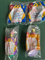 Front view of four 1996 McDonald's Sky Dancers Happy Meal toys in original sealed packaging, with visible label text and toy numbers 1 (two versions), 3, and 4.