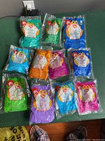 Top view photograph of the 11 original packaged TY Beanie Baby Happy Meal toys arranged on a green surface showing colorful numbering and branding.