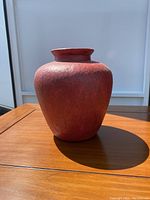 Red textured ceramic vase on wooden table with white backdrop, front view showing shape and texture.