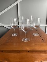 Set of 5 Lucaris red wine glasses arranged on wooden table, showcasing shape and size of large bowls with thin stems.