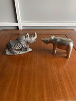 Front view of both rhino figurines, stone rhino on the left, metal rhino on the right, showing textures and shapes.