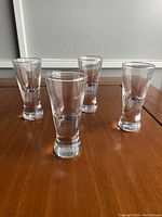 Four clear glass shot glasses arranged on a wooden table showing their height and shape