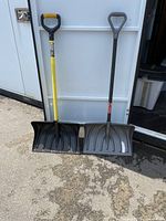 Two snow shovels side by side with different handles and blades leaning against a wall.