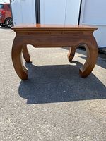 Close-up image of teak wood table with curved legs, showing wood grain and finish