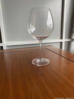 Single Waterford Robert Mondavi Merlot red wine glass on wooden table near window showing full profile.