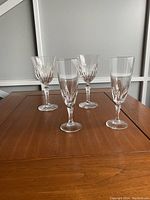 Four glasses on a wooden table: two champagne flutes with swirling bowl patterns, two wine glasses with cut bowl designs.