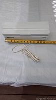White Decosonic food sealer approximately 11 inches long with attached white power cord on white surface with measuring tape for scale.