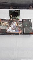 Photo showing three boxed items on a table: golfer's pool game, golf putter return device, and golf-themed picture frame with golf figurines