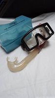 Clear diving mask with black frame, snorkel with clear mouthpiece and red tube, and blue carrying case labeled Dacor
