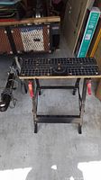 Front view of the Job Mate folding work bench showing black metal folding legs and grid-marked surface with clamp handles.